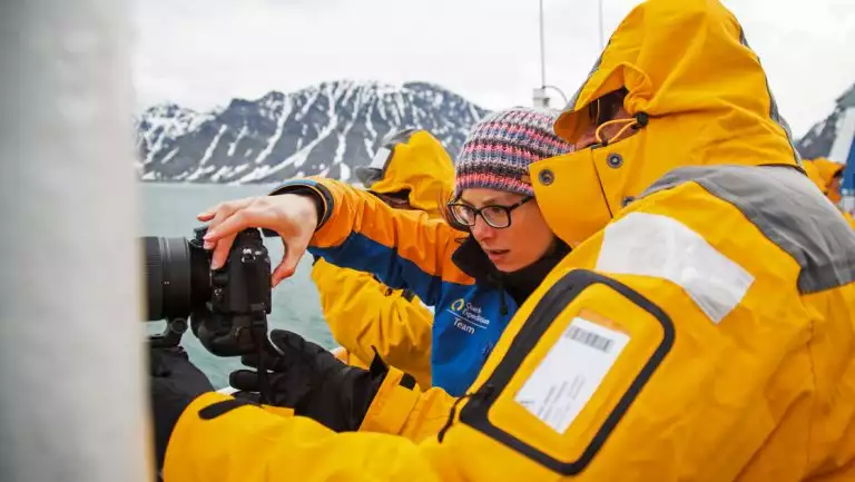 Arctic traveler in yellow jacket looks at camera with photo guide on ship deck on the Spitsbergen Photography cruise.