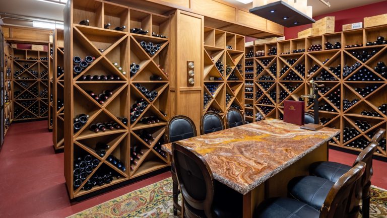 Wine cellar at Captain Cook Hotel with red marble table, blue padded chairs & triangle-patterned wood shelves holding bottles.