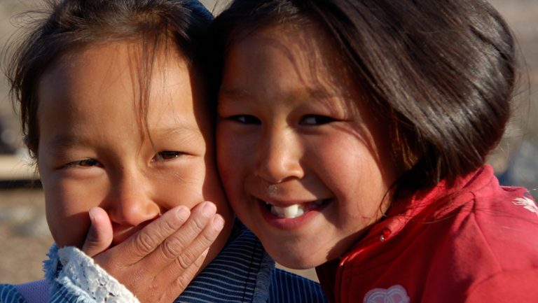2 Inuit girls laugh & smile, seen on Le Commandant Charcot Inuit Spring in Ammassalik small ship cruise in northeast Greenland.