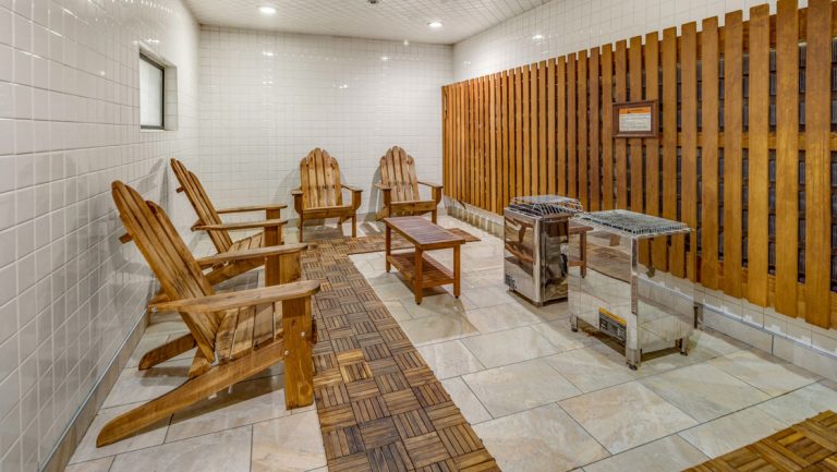 Sauna at Hotel Captain Cook with 4 wood Adirondack chairs, stone floor, wood & tile walls, small window & silver heaters.