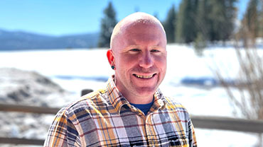 Portrait of Kiel Sprague in a plaid shirt with snowy background and a fence