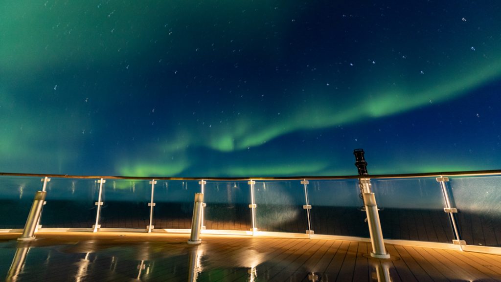Green streaks across dark blue sky seen off the bow of a small ship on the Northern Lights Explorer cruise in the Arctic.