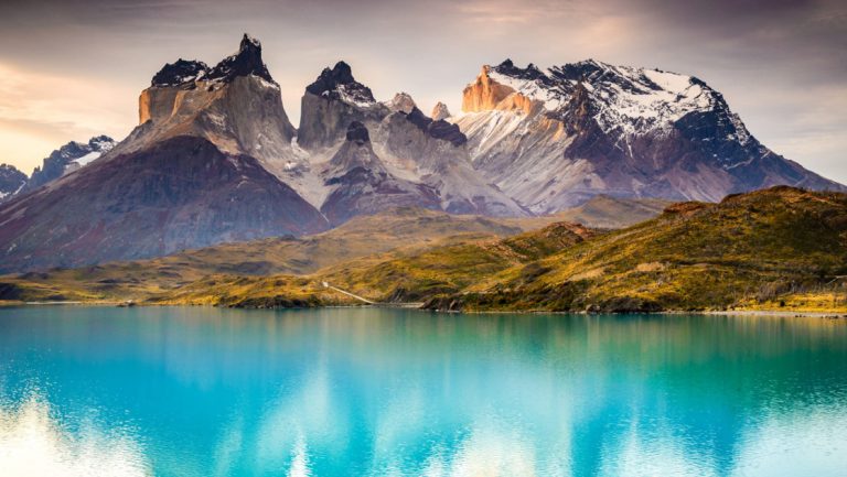 Turquoise lake with golden hillside & jagged peaks behind, seen in Torres del Paine on a Patagonia & Chilean Fjords Cruise.