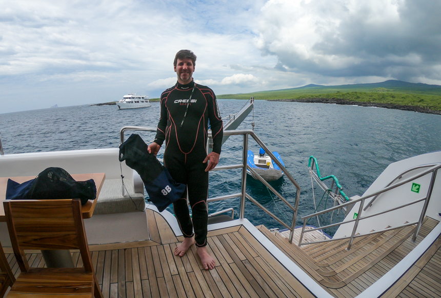 male traveler standing on back deck of ship wearing black and red wetsuit for snorkel activity aboard elite Galapagos cruise