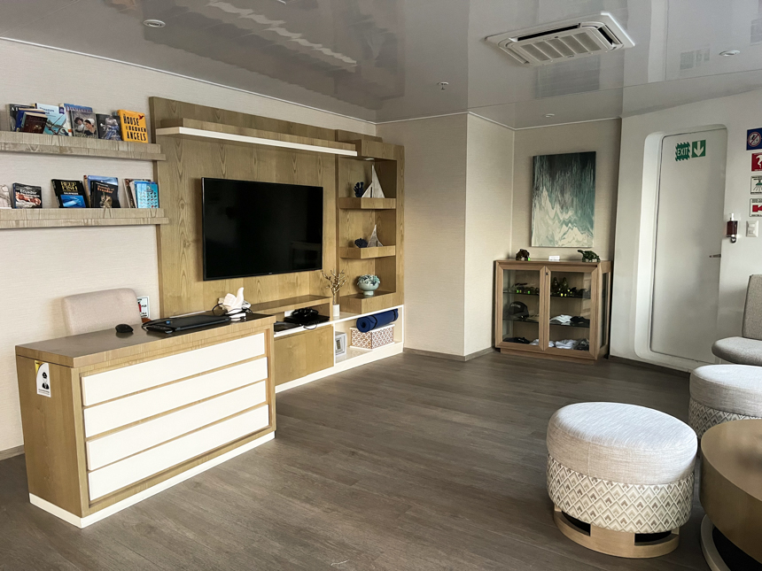 Social area aboard Endemic Galapagos cruise ship, flat screen tv on wall with books, and chairs with ottomans.