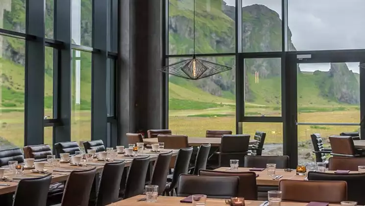 Dangar restaurant in south Iceland's Hotel Kria with walls of glass looking onto green hills, modern furniture & lots of seating.