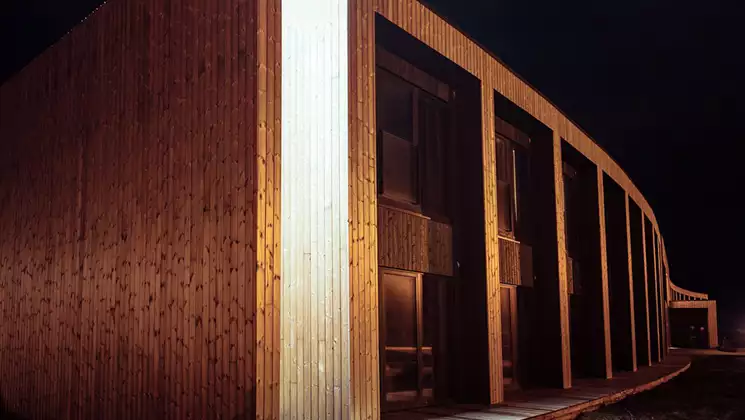 Nighttime exterior of Hotel Kria in Vik, Iceland, with modern, clean lines, wood, tall insets & rounded facade.