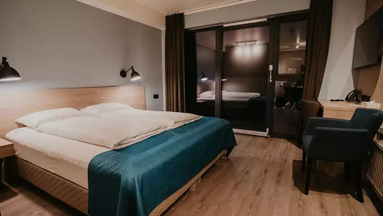 Guest room at Hotel Kria in Iceland, with double bed in white & teal linens, desk, bedside lights, wood floors & big windows.