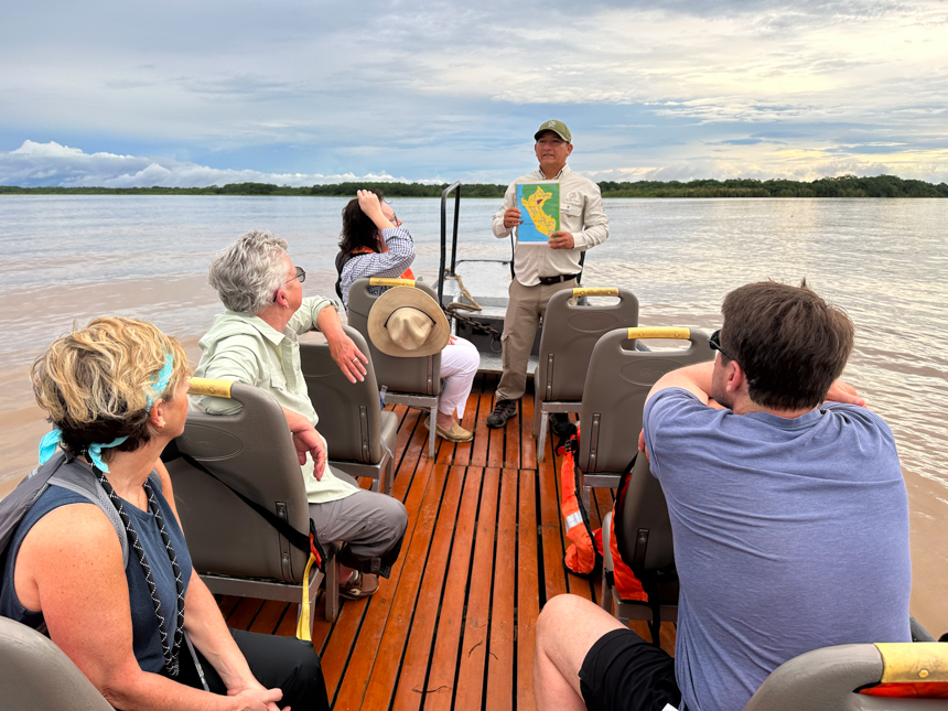 From the back of the skiff 4 guests face the naturalist guide who is at the front holding a map giving a talk.