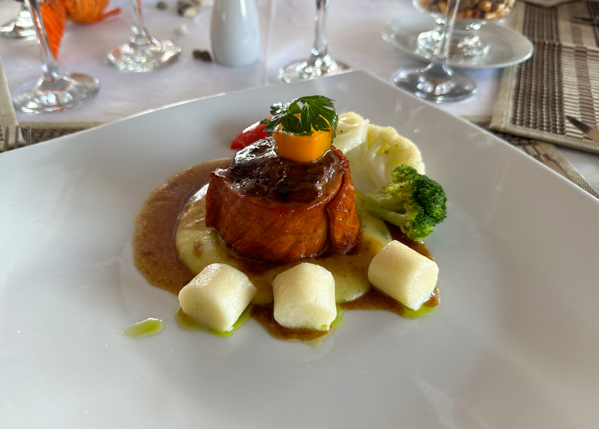 Food aboard delfin, a pink and brown steak with sauce and brightly colored vegetables are served on a white plate 