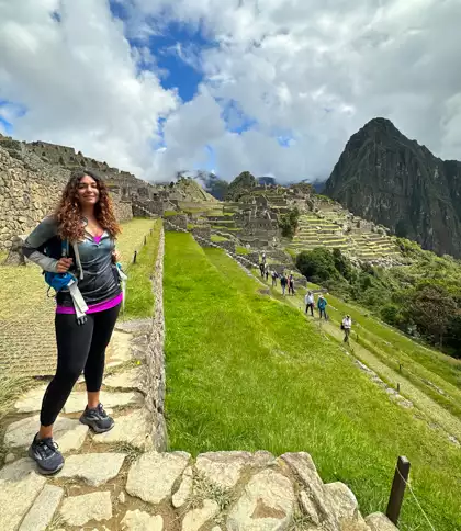Female AdventureSmith staff member standing on rock staircase with Machu Picchu citadel ruins behind her in Peru.