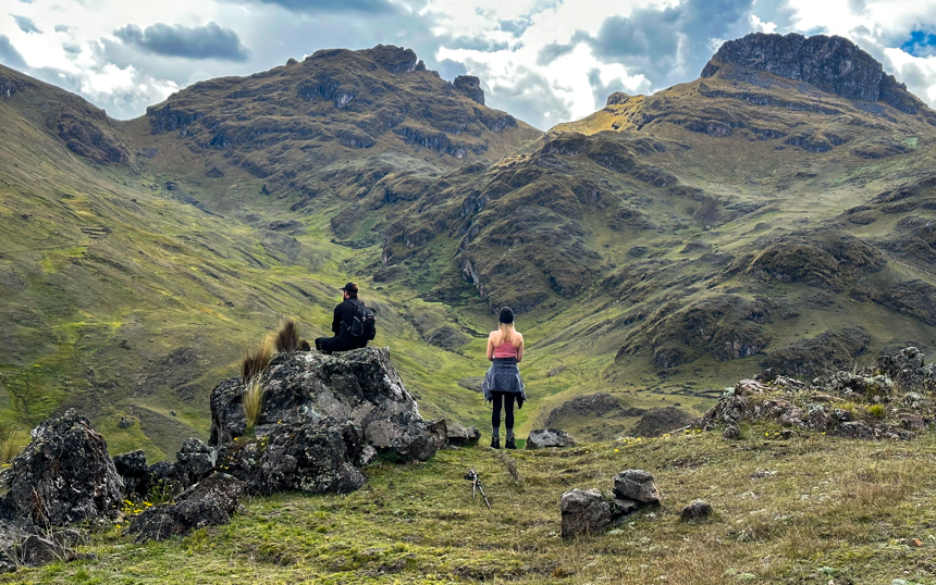 Two travelers take in the scenery from their Paru hike in Peru's Sacred Valley. Jagged, rocky green mountain scope on cloudy day