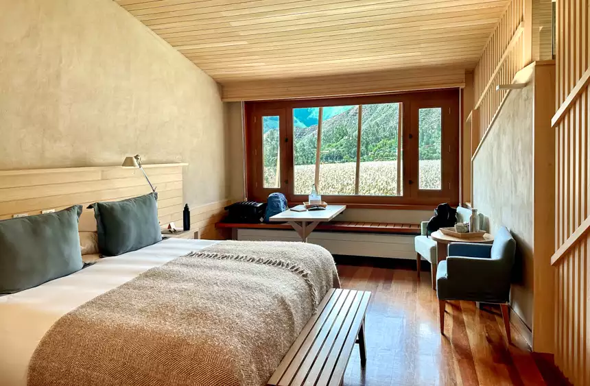 Explora Sacred Valley Lodge in Peru standard room, with window to corn field, two tables. two chairs and queen bed.