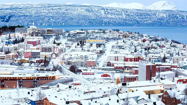 Aerial view of snow-covered Norwegian town by calm blue sea, seen on the Nordic Discoveries & Traditions cruise.