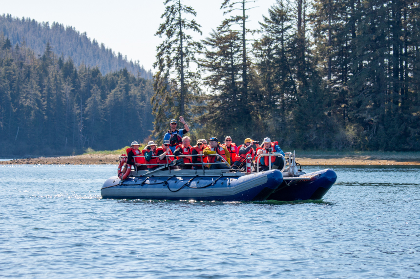 Guests in orange life jackets ride an inflatable skiff through the waters of Alaska as part of a small ship cruise activity. 