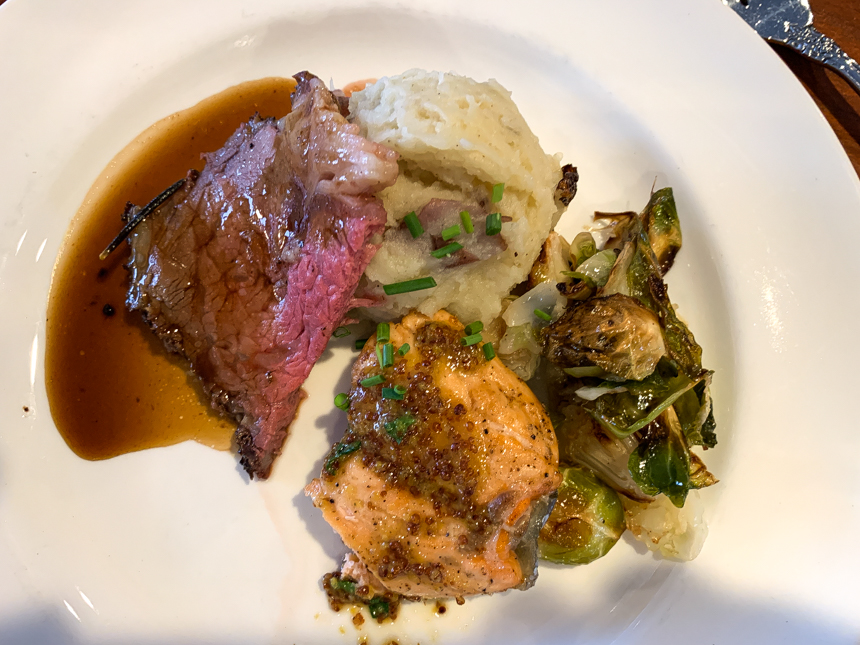 Steak with mashed potatoes and gravy with green Brussel sprouts with green chives on top.