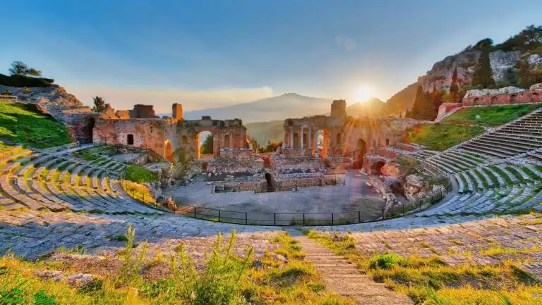 Ancient theatre of Taormina Siciliy Italy with Etna erupting volcano at sunset, seen on cruises around Sicily and Malta.
