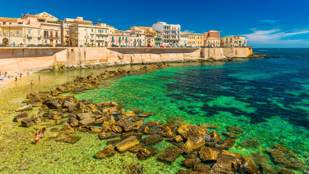 Cityscape of Ortygia. City beach in the historical center of Syracuse, on Sicily, Italy, with rocks & turquoise water.