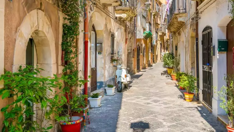 Picturesque stone street in Ortigia, Siracusa old town, Sicily, southern Italy, with white moped & green door plants.