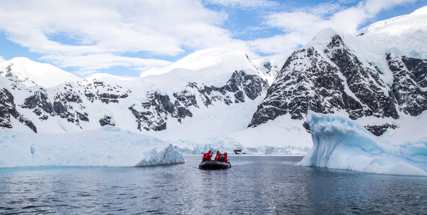 Antarctica in October is pristine with  white-capped peaks and large icebergs A group of guests ride an inflatable skiff through the water.