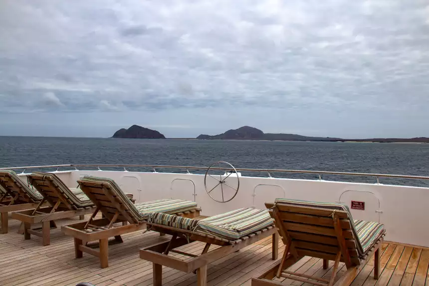 Wooden lounge chairs with green pads set out on top deck of seaman journey overlooking the ocean and islands in distance. 