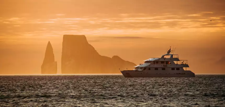 A deep orange sunset over a silhouetted kicker rock and Seaman Journey floats on the horizon line in the Galapagos. 