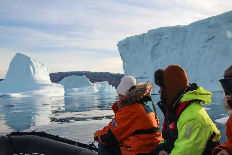 In East Greenland guests wearing orange and green parkas take a skiff ride through huge icebergs in Scoresby Sund. 