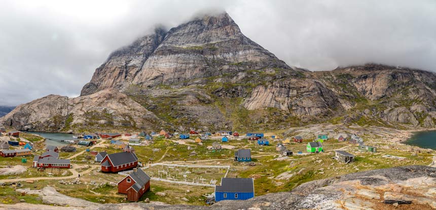 Bright and colorful wood houses of the small Greenland village of Aappilattoq set against jagged mountains. 