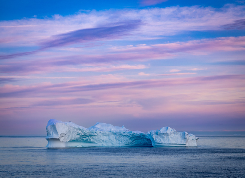 Seen from a Greenland cruise, Massive iceberg sculpture floating in the ocean during a pastel sunset of pink purple and blue 