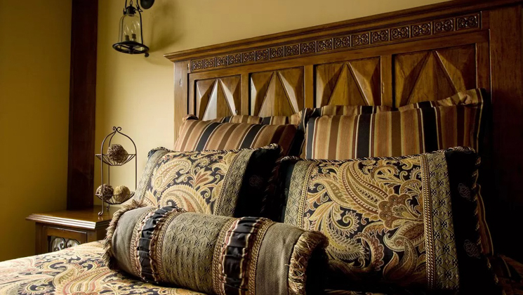 Double bed with paisley throw pillows & bedding & carved wood headboard with bedside table at the Homes at Kenai Riverside Lodge.