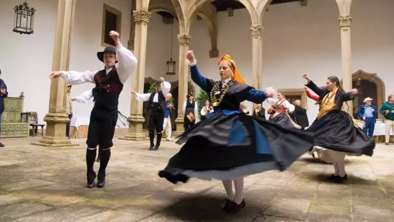 Women twirl in black dresses as men raise arms beside them in a dance performance in a Spanish building's stone courtyard.