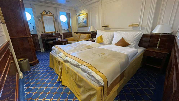 Category 1 cabin on Sea Cloud II: Lindblad ship with 2 single beds pushed together in gold & blue motif & 2 portholes.