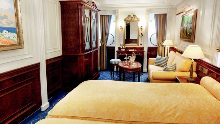 Category 2 cabin on Sea Cloud II: Lindblad ship with 2 single beds pushed together & couch in gold motif & 2 portholes.