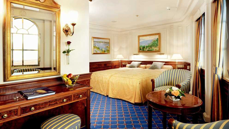 Category 4 cabin on Sea Cloud II: Lindblad ship with 2 single beds pushed together in gold, wood & blue motif & large windows.