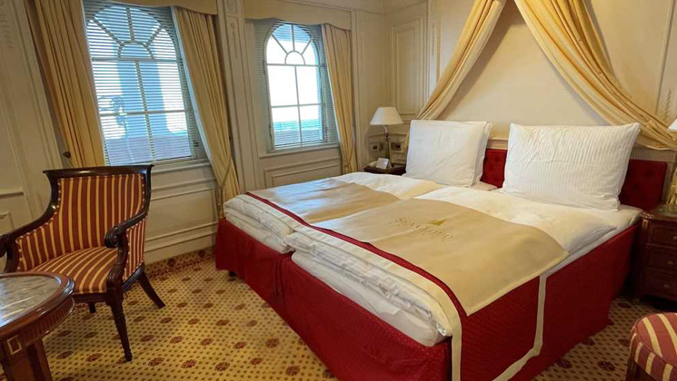 Category 5 cabin on Sea Cloud II: Lindblad ship with 2 single beds pushed together in red, white & gold motif & large windows.