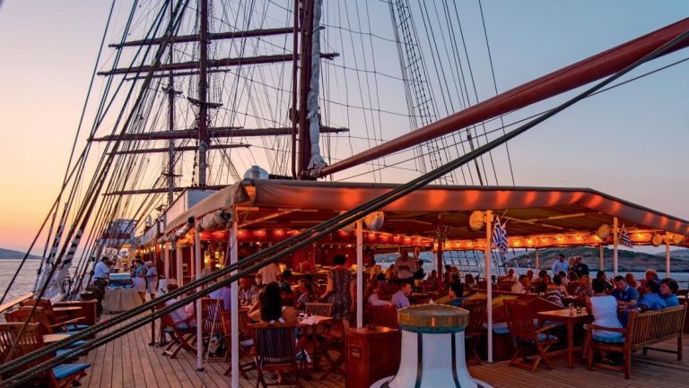 Sea Cloud II: Lindblad tall ship at sunset with open-air Lido Deck bar lit up & guests sitting & sipping.