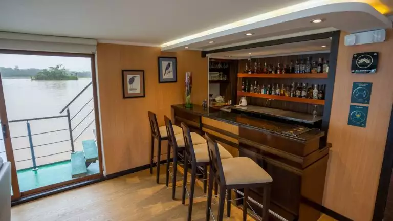 Bar aboard small cruise ship with barstools and places to relax next to large window