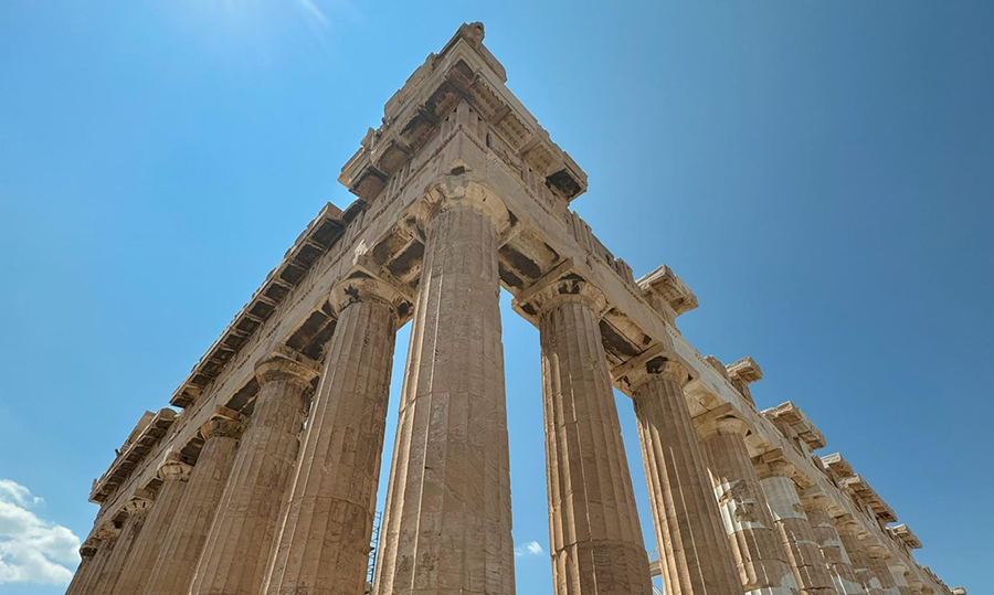 Looking up at a corner of the Parthenon in Athens Greece with ancient columns stretching into a blue sky.  