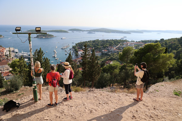 Hvar Croatia seen from above with four travelers standing on a hilltop above the town taking pictures