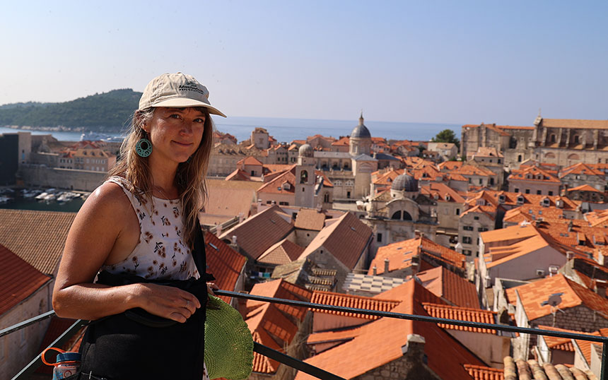 A woman in a tan AdventureSmith hat stands on the Dubrovnik old city walls with many red roofs behind her