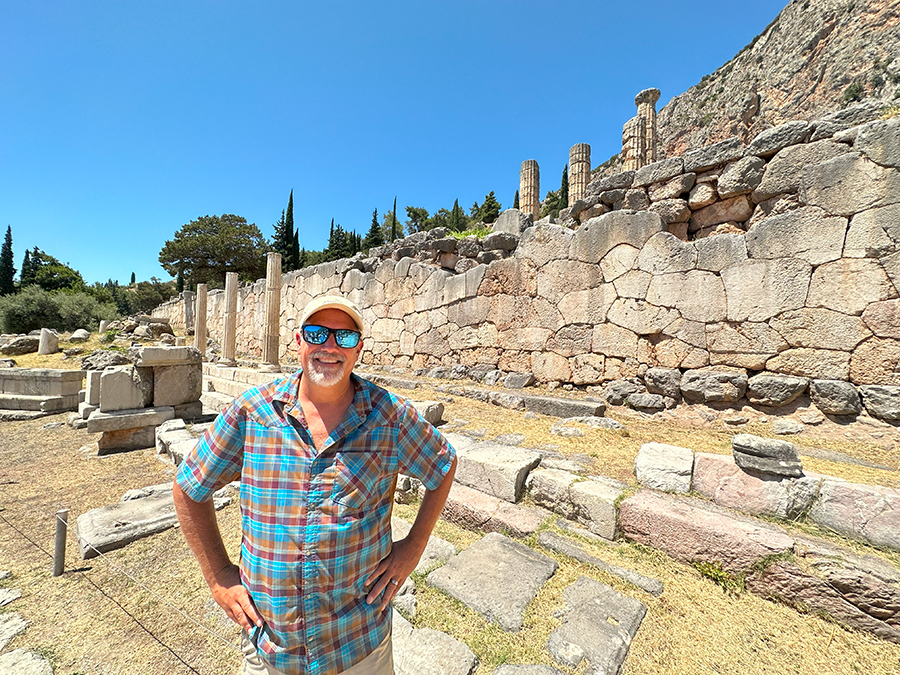A male traveler standing in front of ancient ruins in Greece. 