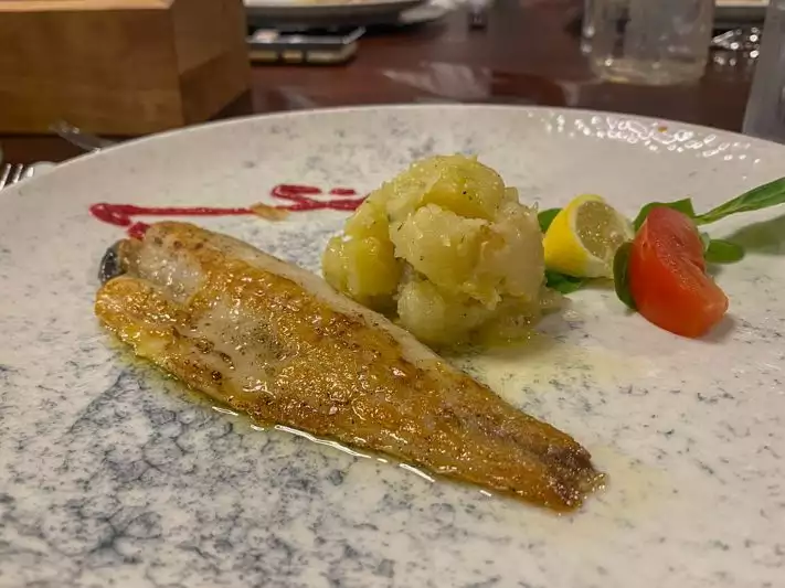 A plate showing a filet of white fish, mashed potatoes, a tomato and lemon slice 