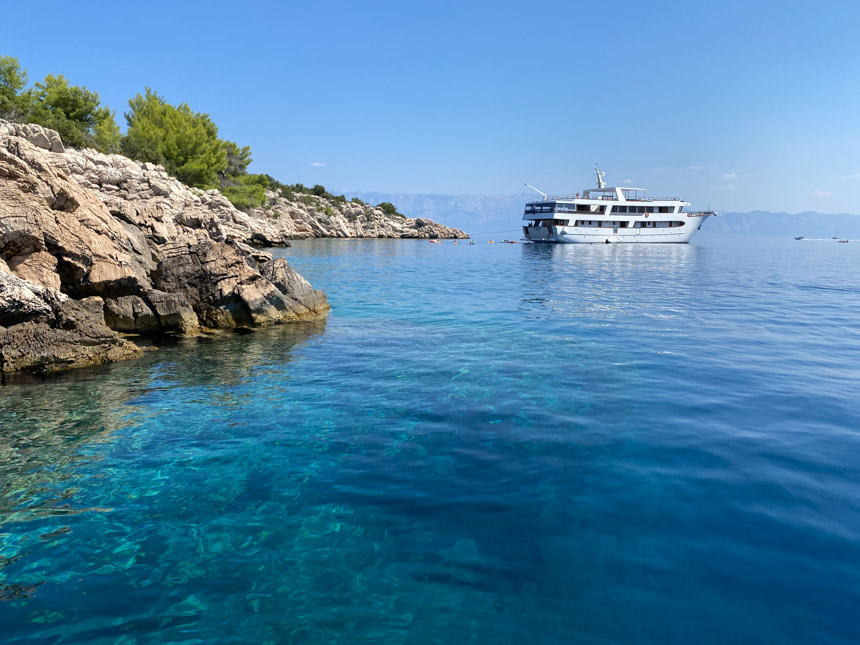 A white yacht seen at anchor in the clear Adriatic Sea by a rocky shoreline