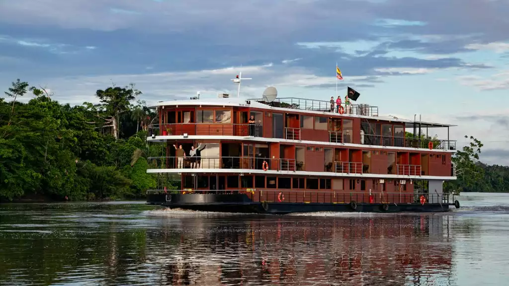A red river boat cruising down the amazon river surrounded by calm waters and green bush