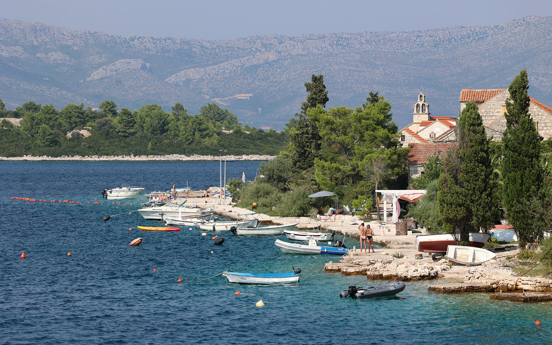 A view of a shoreline in Croatia with vacationers and boats on the rocky shoreline