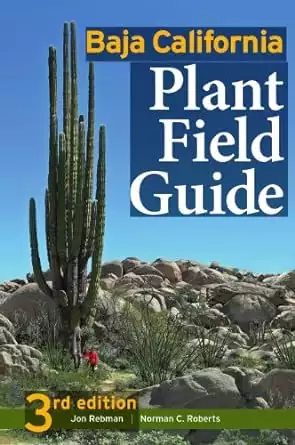Book cover of Baja California Plant Field Guide with a person in a red shirt standing next to a massive tall cactus in a rocky landscape with blue sky. 