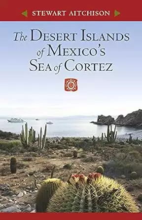 Book cover of the Desert Islands of Mexico's Sea of Cortez by Stewart Aitchison showing a desert landscape with large cactus a calm bay with two boats anchored. 