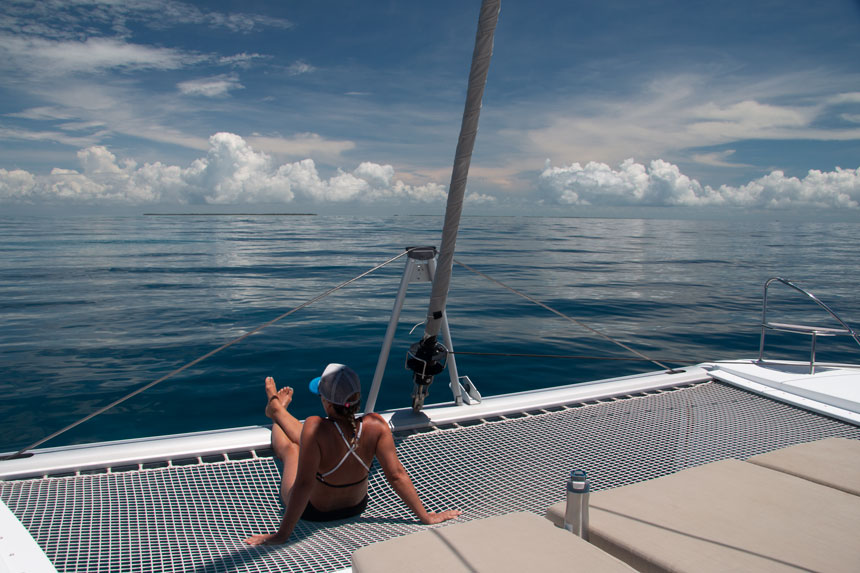 a female traveler in a bikini lounging on the netted front canopy of a sailing catamaran cruising in Belize. 