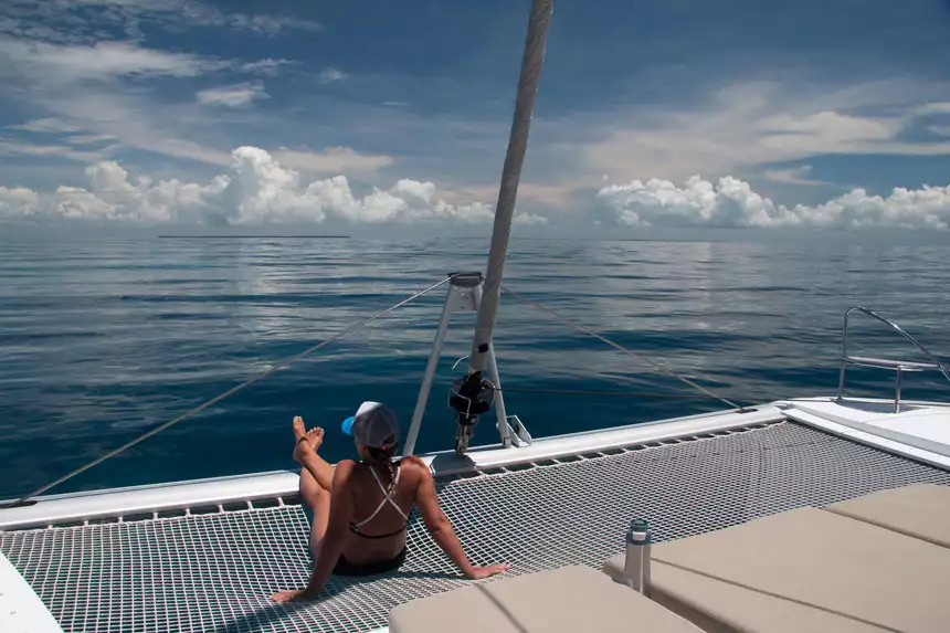 a female traveler in a bikini lounging on the netted front canopy of a sailing catamaran cruising in Belize. 
