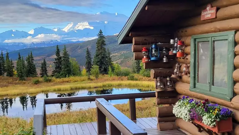 Pond outside a log cabin at Camp Denali, with a view of the Alaskan wilderness with mountains, tundra & boreal forest.